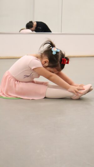 Little ballerina stretching on dance studio floor