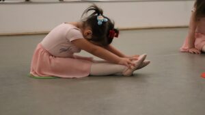 Young ballerina in pink stretching on floor